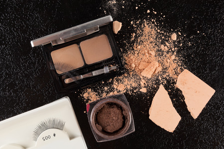 Beige and brown natural make up, foundation, eye shadow on black table, flat lay.