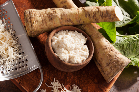 Fresh and grated horseradish with leaves on wooden background from above. Healthy vegetable.の写真素材