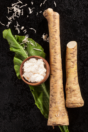 Whole and grated horseradish with leaves on black background from above. Healthy vegetable.の写真素材