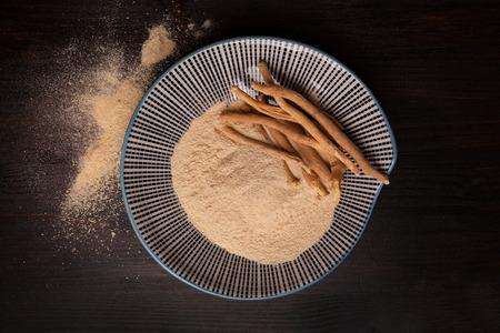 Ashwagandha powder and roots on plate on black background from above. Superfood, adaptogen,...