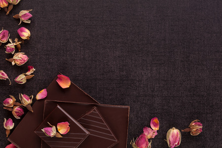 Luxury chocolate bars with dried rose on black background from above.