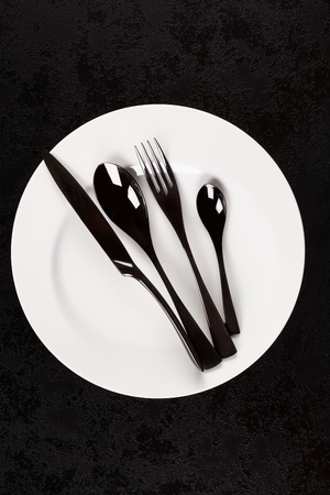 Black cuttlery on white plate from above on dark surface. Modern design concept.の写真素材
