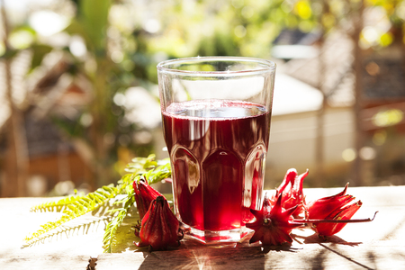 Roselle tea glass with fresh roselle fruit on wooden table, healthy herbal drink concept. (karkade, red sorrel, Agua de flor de Jamaica)の写真素材