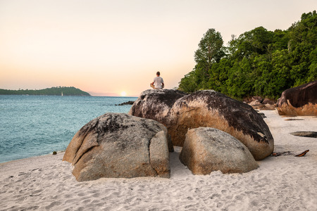 Young Man Meditating and doing Yoga Exercises against beautiful ocean view on stones.の写真素材