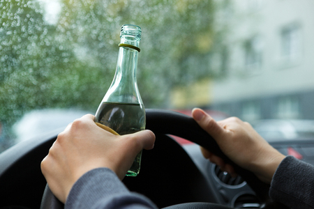 Close up of driver and drinking alcohol. Young woman driving a car with a bottle of wine. Don't drink and drive concept. Driving under the influence, DUI.の写真素材