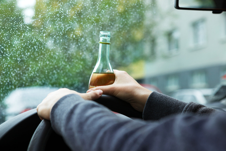 Close up of driver and drinking alcohol. Young woman driving a car with a bottle of wine. Don't drink and drive concept. Driving under the influence, DUI.の写真素材
