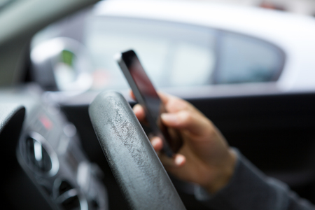 Woman sitting in the car and texting on touch phone with black screen. Dangerous driving.の写真素材