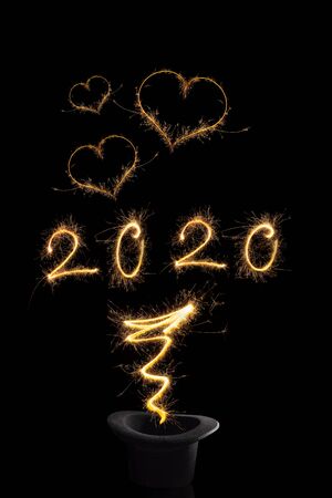 Magical happy new year. Magical fireworks from black top hat forming digits 2020, heart shapes and abstract light lines isolated on black background. Happy new year background.の写真素材