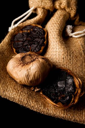 Black garlic on black plate on dark background from above. Culinary food ingredient.の写真素材