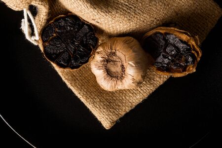 Black garlic on black plate on dark background from above. Culinary food ingredient.の写真素材