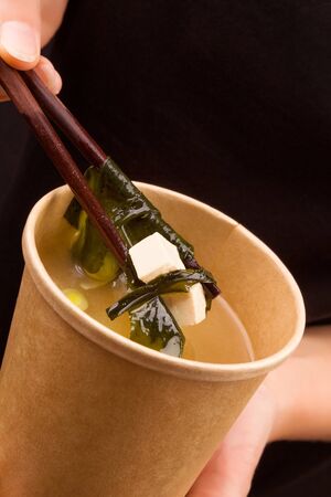 Woman eating miso soup in takeaway cup. Traditional asian cousine.の写真素材