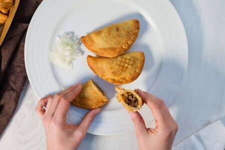 Traditional baked Argentinian empanadas savoury pastries with meat beef stuffing with fresh onion on white plate from above.の写真素材