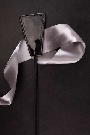 Black whip flogger and silver ribbon on leather background. Sex toy.の写真素材