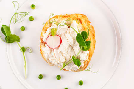 Tasty bread with cream cheese, peas and radish on white plate from above.の写真素材