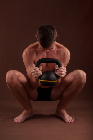 Handsome muscular adolescent shirtless boy training in deep squat exercise with kettlebell.の写真素材