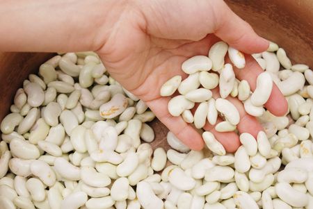 Detail of woman hand riddling in white beans           