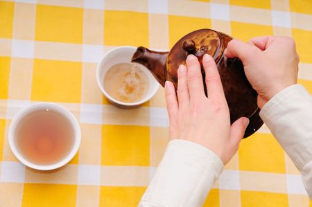 Hands hold tea pot and pour tea into cup - upper view