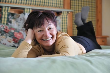 Smiling senior woman lying on bed in hotel room and relaxing        の写真素材