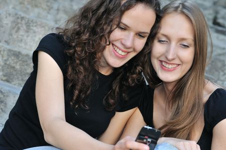 Youth lifestyle - two smiling friends (girls) outdoors with mobile phoneの写真素材