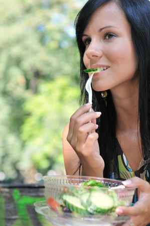 Young beautiful woman having lunch break and eating salad outdoors in parkの写真素材