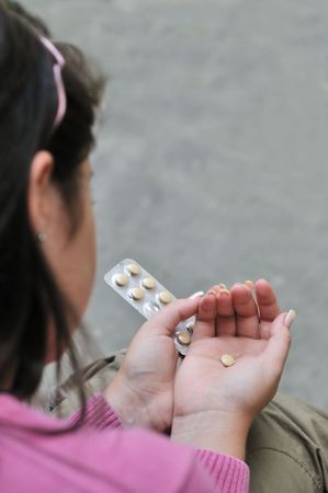 Take or not - young woman  (teenage girl) decides while holding pills, focus on handsの写真素材
