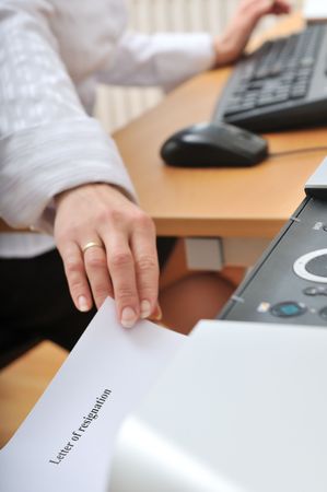 Hand of business woman reching paper (letter of resignation written on) from printer on workplaceの写真素材