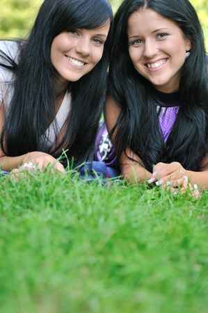 Two smiling friends lying together in grass outdoors with copy spaceの写真素材