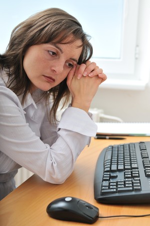 Young frustrated and depressed business person (woman) sitting at table with computerの写真素材