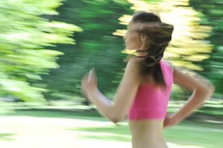 Young person (woman) running outside in park on sunny day - motion blurr                  の写真素材