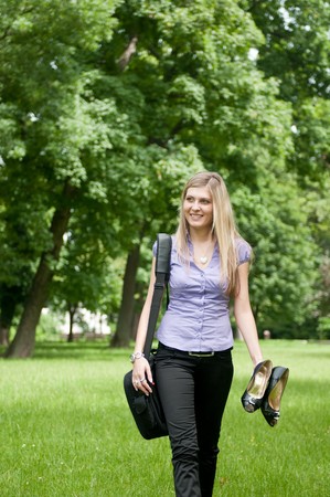 Young business woman wit laptob bag walking outdoors in park and holding shoesの写真素材