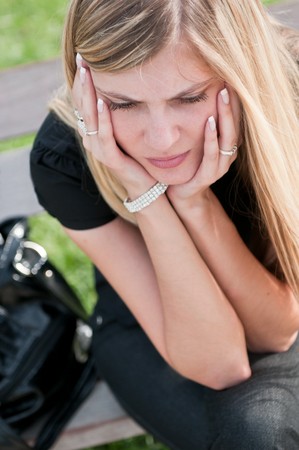 Young worried beautiful woman siting on bench - head in handsの写真素材
