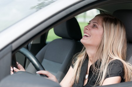 Young beautiful laughing woman driving car - portrait through side windowの写真素材