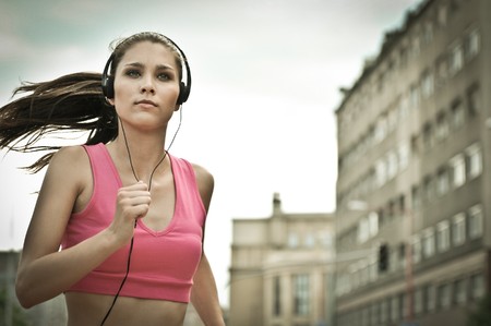 Person (young beautiful woman) listening music running (jogging) in city streetの写真素材
