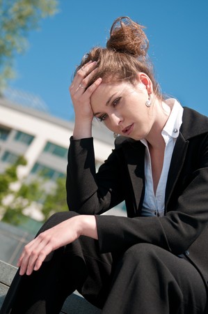 Young depressed business woman siting outdoors - building in backgroundの写真素材