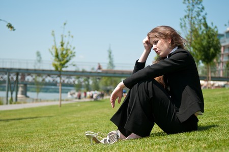Young worried business woman siting outdoors in grass - head in handの写真素材