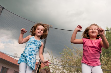 Small cute children jumping on trampoline - garden and family house in backgroundの写真素材