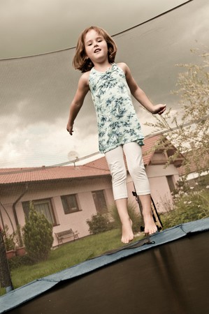 Small cute child jumping on trampoline - garden and family house in background (sepia tone)の写真素材