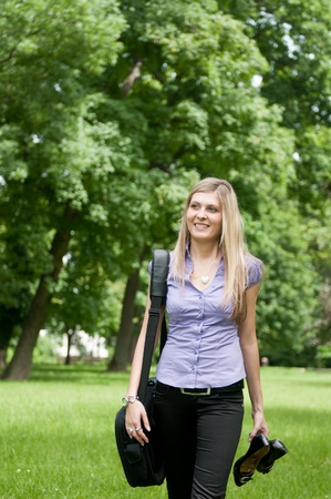 Young business woman wit laptob bag walking outdoors in park and holding shoesの写真素材