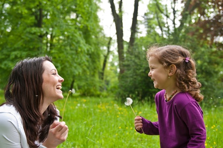 Mother with small daughter laughing  after blowing to dandelion の写真素材