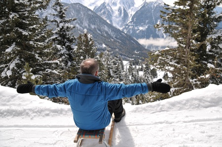 Senior man on sledge having fun in mountain snowy countryの写真素材