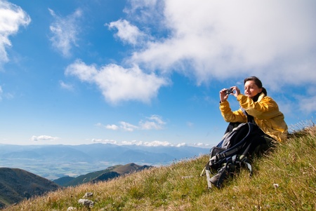 Young person relaxes on hiking in mountains and taking photo with mobile phoneの写真素材