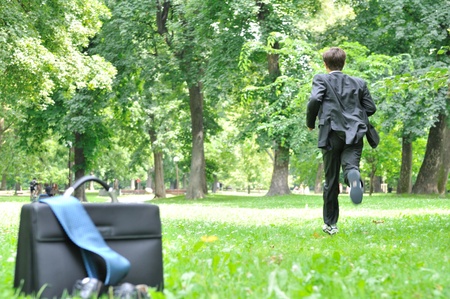 Escape from civilization concept - business man running in park away from bag, shoes and tieの写真素材