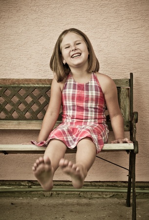 Portrait of cute child sitting on bench and stretching barefoot legs - sepia toningの写真素材