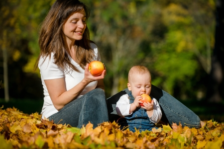 Beautiful baby with mother eating apples outdoor in natureの写真素材