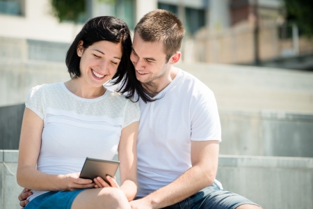 Young happy couple smiling over something in tablet - outdoorの写真素材