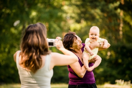 Mother taking photo of grandmother holding her granddaughter - outdoor in natureの写真素材