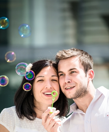 Young couple have great time together with bubble blower - outside in streetの写真素材