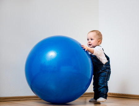 Little baby is playing with big blue fit ball at homeの写真素材