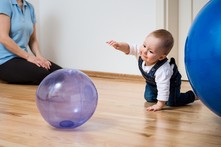 Baby plays with inflatable ball at home on floor, mother in backgroundの写真素材