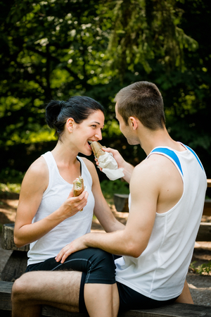 Young couple eating after sport training outdoor in nature - man feeds womanの写真素材